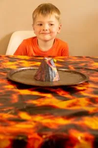 model lava volcano in the middle of the table, boy looking on.