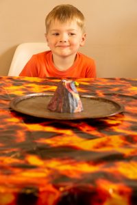 model lava volcano in the middle of the table, boy looking on.